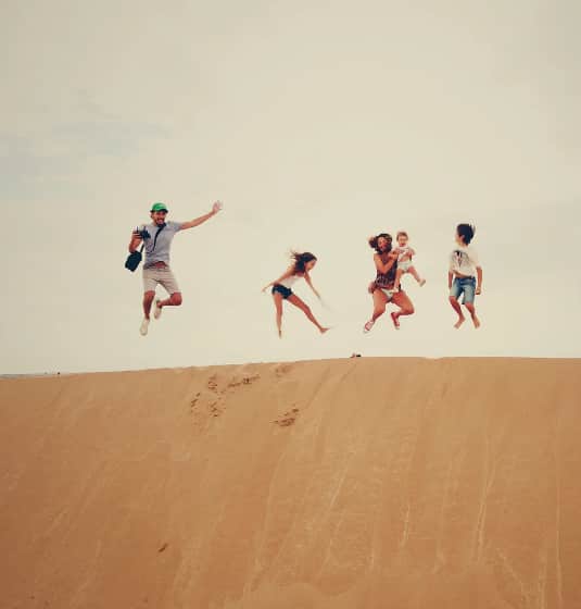 sc-cs-booking-hero A family jumping on the sand