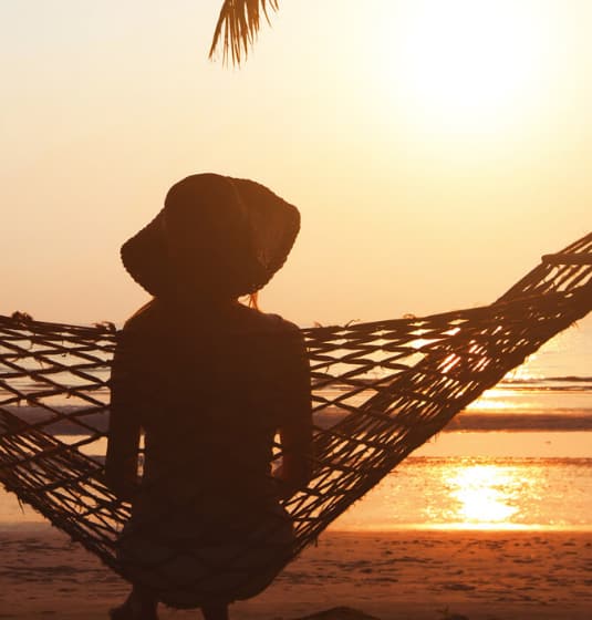 sc-cs-lastminute-hero A woman sitting in a hammock looking out to sea